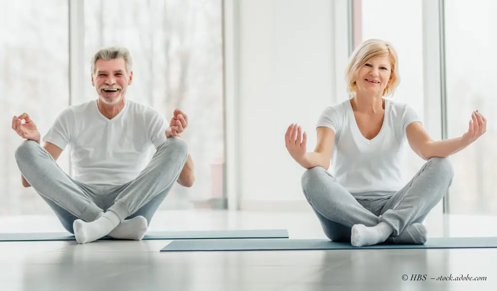 Beim Yoga für Senioren machen ein Mann und eine Frau eine Übung auf dem Boden